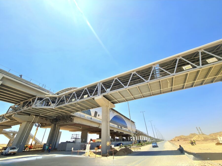 A pedestrian bridge, spanning over a busy road and connected to an elevated, monorail station.
