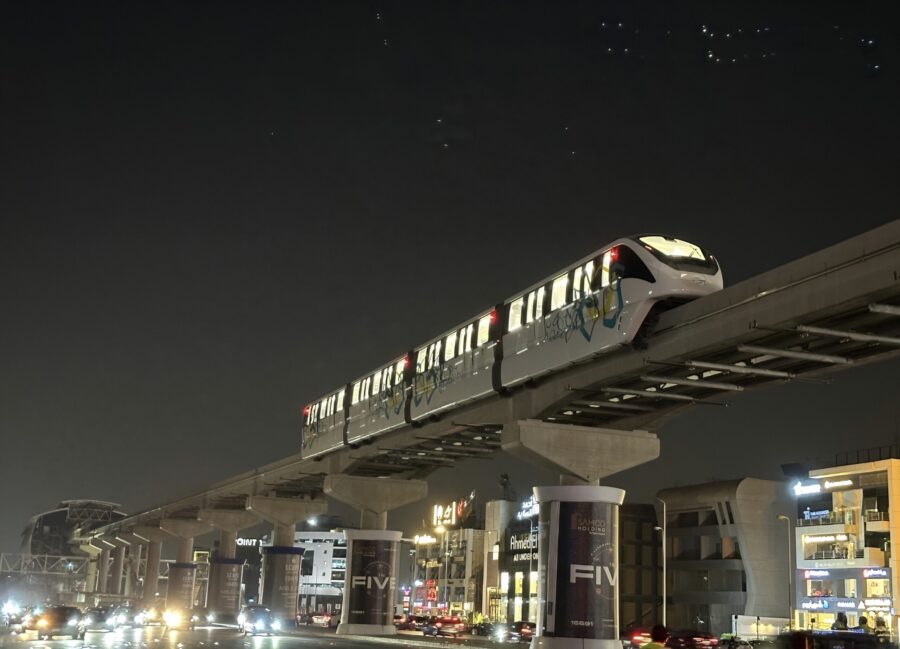 A monorail train traversing across a sky rail over a street at night.