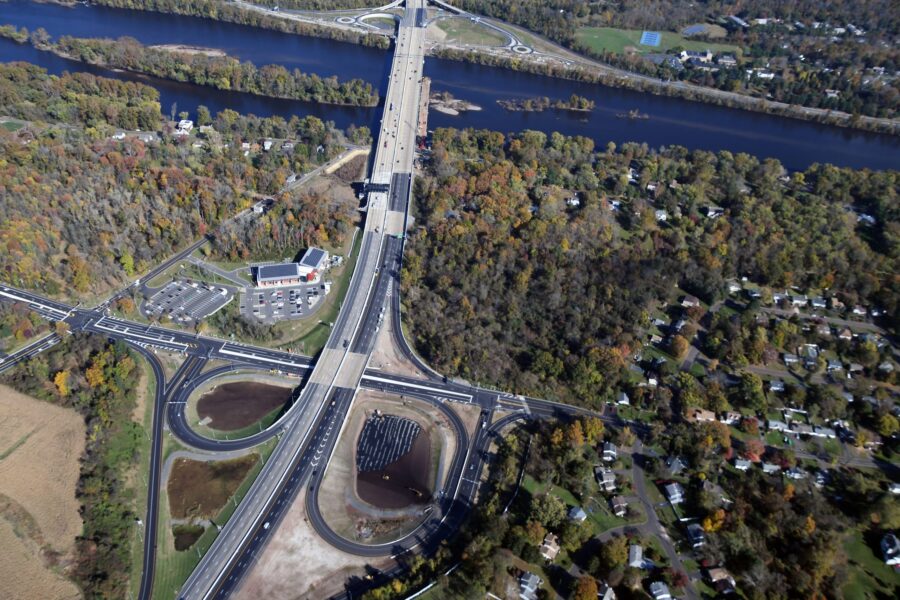 An arial shot of a highway bridge interchange in the middle of Semi-wooded area.