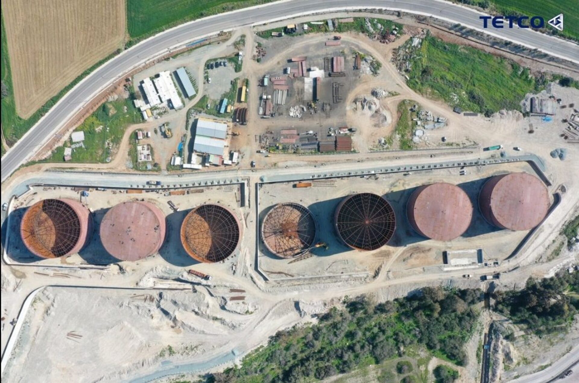 A satellite view of seven large metal silos, three of which are completed and the remaining four are still in construction.