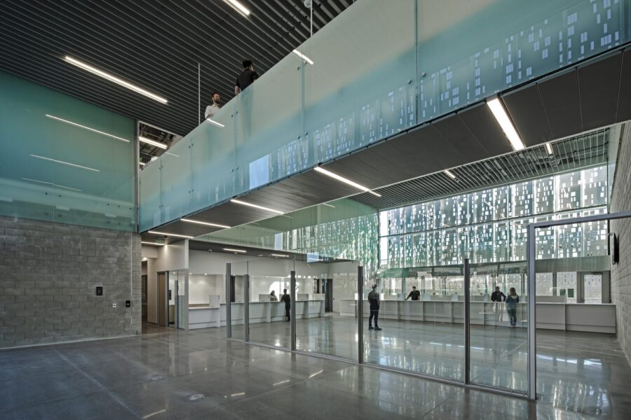 A large room featuring a glass wall and suspended bridge made of steel and glass, with a standing reception desk in the far wall.
