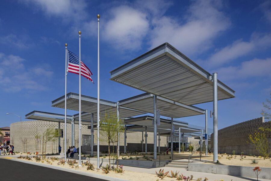 The front of a building that features a small, covered gravel courtyard and three flag poles