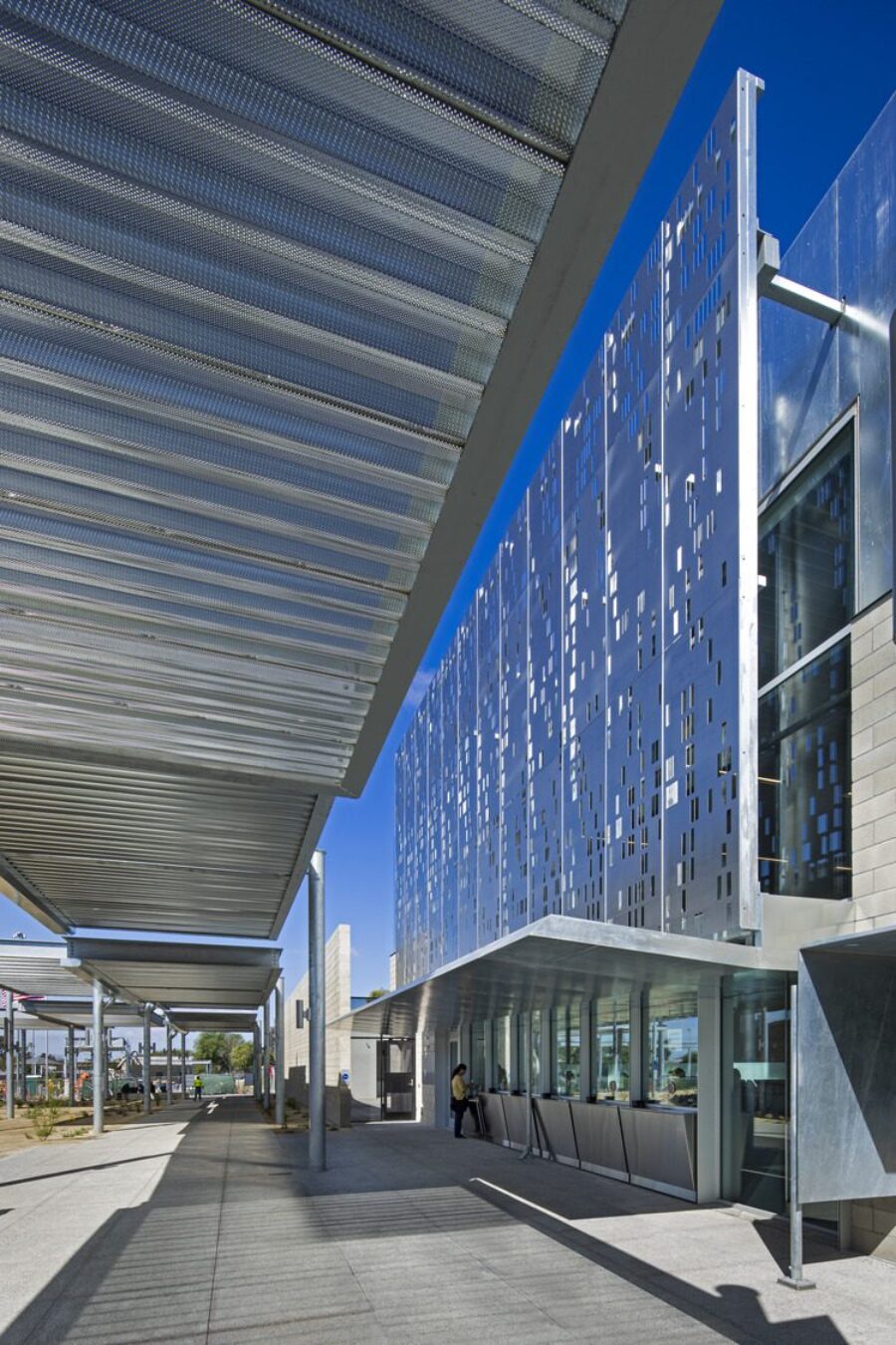 The front of a building with a large metal feature and a covered walkway running across the entrance.