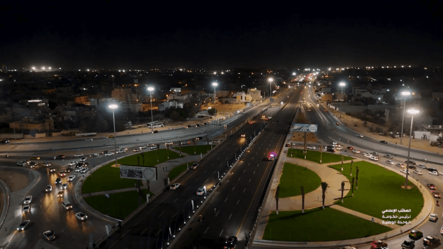 A section of large freeway, flanked by small, semi-circular parks, at night.