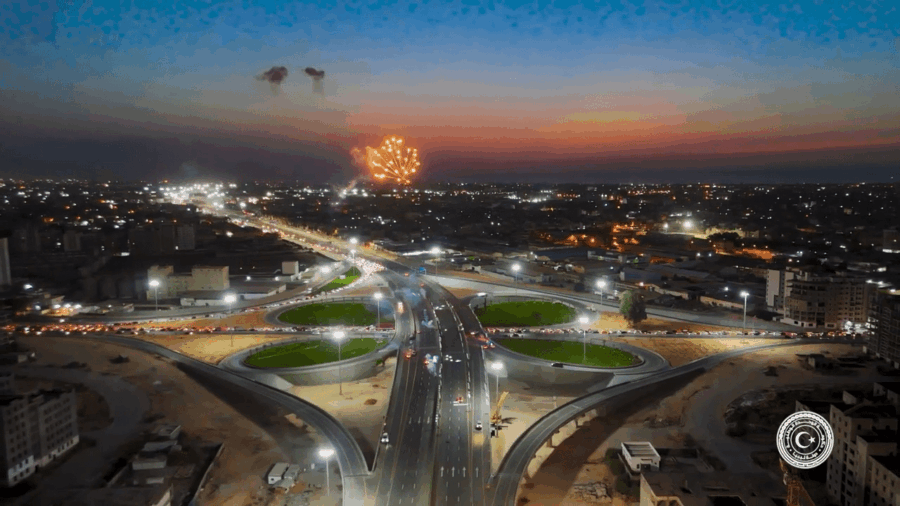 A large freeway intersection in the middle of a city, at sunset with fireworks in the air.
